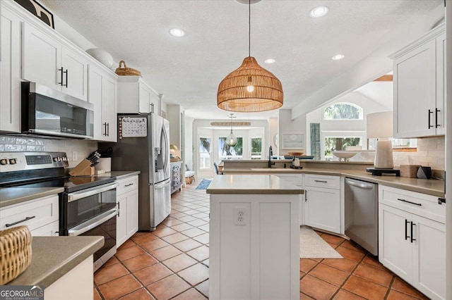 kitchen with decorative light fixtures, stainless steel appliances, backsplash, white cabinets, and a kitchen island