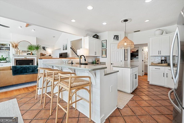 kitchen featuring decorative light fixtures, freestanding refrigerator, open floor plan, white cabinetry, and an island with sink