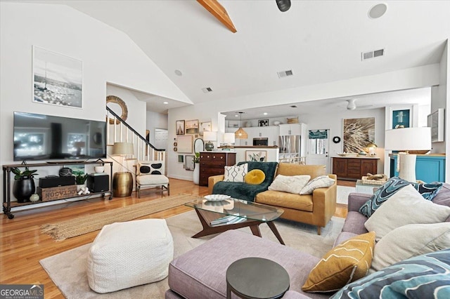 living area featuring stairs, high vaulted ceiling, light wood-style flooring, and visible vents