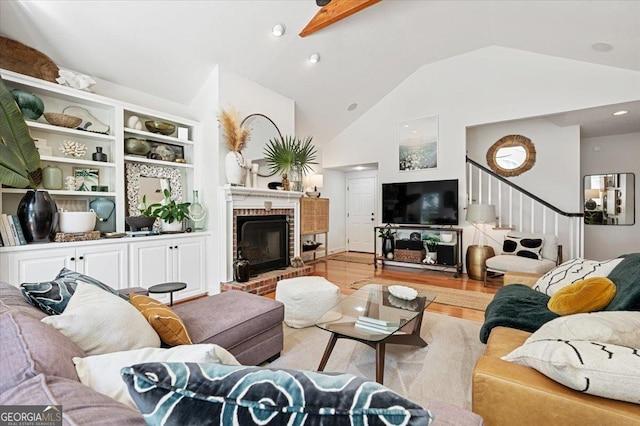 living area with stairs, light wood-type flooring, a brick fireplace, and high vaulted ceiling