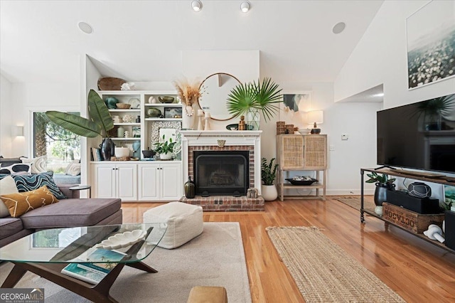 living area featuring high vaulted ceiling, a brick fireplace, baseboards, and light wood finished floors