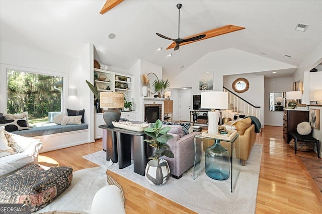 living area with ceiling fan, light wood-style flooring, a fireplace, visible vents, and stairs