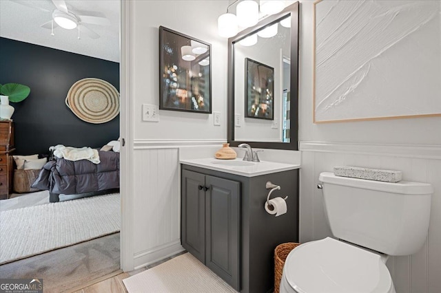 bathroom with toilet, a ceiling fan, wainscoting, connected bathroom, and vanity