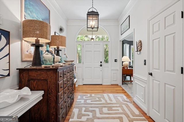 foyer featuring a chandelier, ornamental molding, light wood-style flooring, and a decorative wall