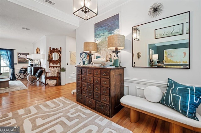 living area with visible vents, wainscoting, light wood-style flooring, an inviting chandelier, and crown molding