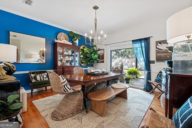 dining room with light wood-type flooring, a textured ceiling, visible vents, and a notable chandelier