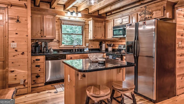 kitchen with sink, a kitchen island, wooden walls, and appliances with stainless steel finishes