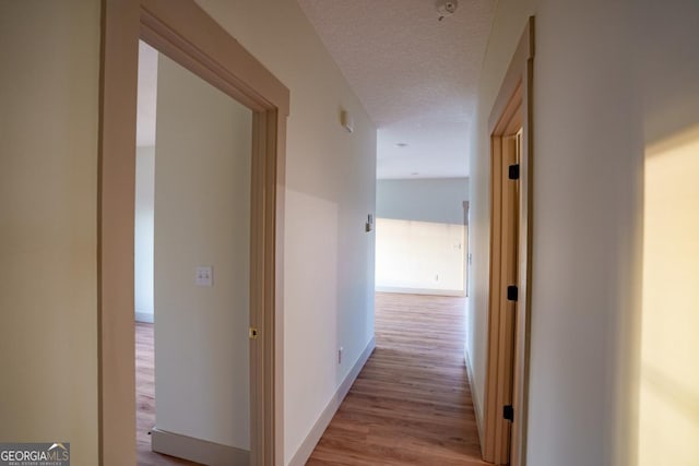 corridor with light hardwood / wood-style flooring and a textured ceiling