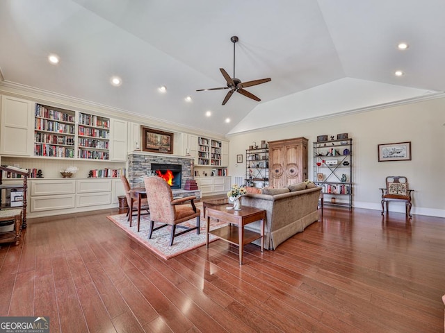 living room with vaulted ceiling, wood-type flooring, built in shelves, a stone fireplace, and ceiling fan