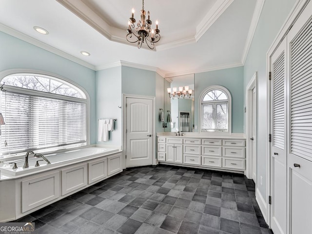 bathroom with a notable chandelier, a tub to relax in, a raised ceiling, ornamental molding, and vanity