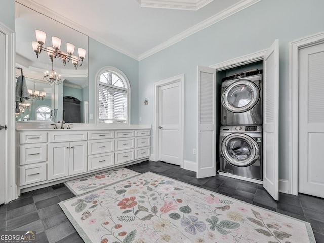 washroom featuring sink, ornamental molding, stacked washer / drying machine, and a notable chandelier