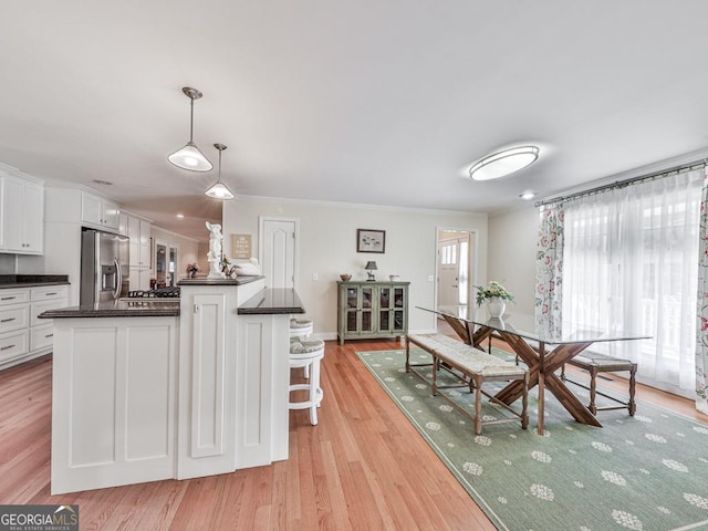 kitchen featuring stainless steel fridge with ice dispenser, hanging light fixtures, light hardwood / wood-style flooring, white cabinets, and a kitchen bar