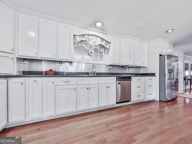 kitchen featuring dark stone countertops, sink, light hardwood / wood-style floors, stainless steel appliances, and white cabinets