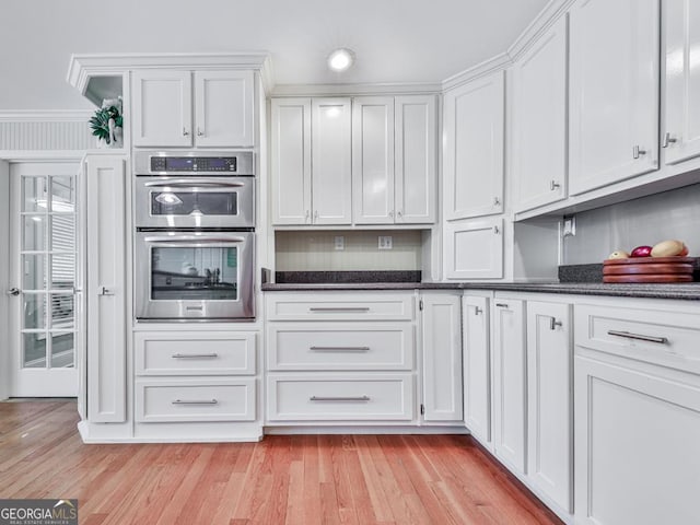 kitchen featuring light wood-type flooring, dark stone countertops, white cabinets, and double oven