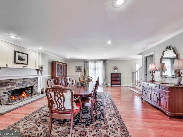 dining area featuring a stone fireplace, crown molding, and light hardwood / wood-style floors