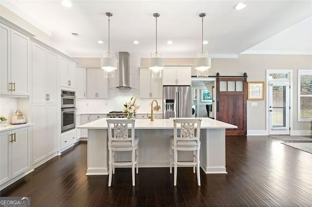 kitchen with pendant lighting, stainless steel appliances, wall chimney exhaust hood, and a barn door