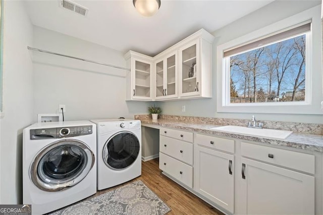 laundry area featuring washer and dryer, sink, cabinets, and light hardwood / wood-style flooring