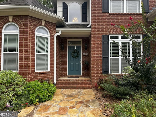 property entrance featuring roof with shingles and brick siding