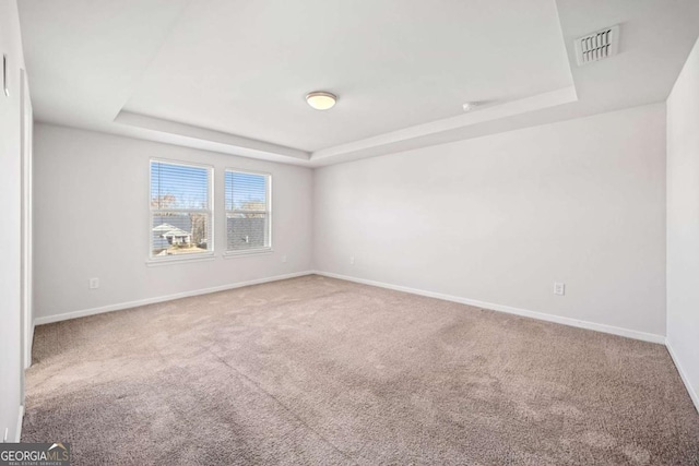 empty room with carpet, a raised ceiling, visible vents, and baseboards