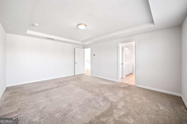 unfurnished bedroom with ensuite bathroom, light colored carpet, visible vents, baseboards, and a tray ceiling