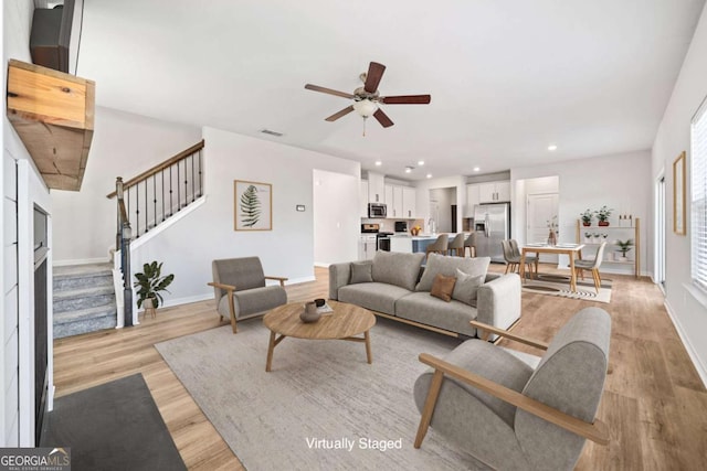 living room with recessed lighting, visible vents, light wood-style flooring, baseboards, and stairs