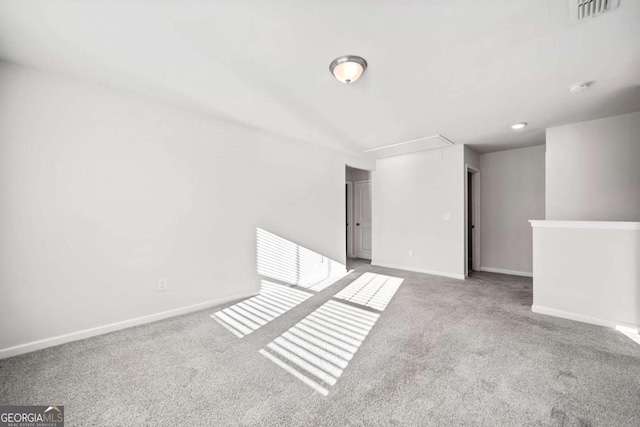 empty room featuring attic access, carpet, visible vents, and baseboards