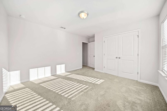 unfurnished bedroom featuring baseboards, a closet, visible vents, and light colored carpet