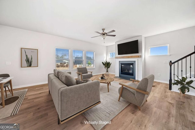 living room with a ceiling fan, stairway, baseboards, and wood finished floors