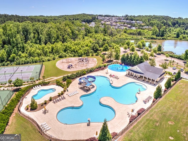 community pool with a patio area, a water view, and a view of trees