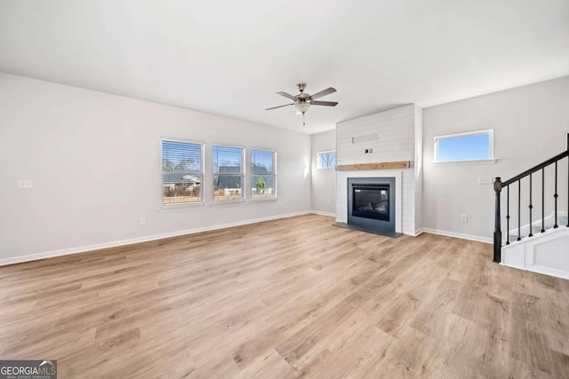 unfurnished living room featuring light wood-type flooring, a brick fireplace, stairs, and baseboards