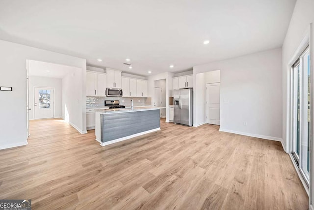 kitchen featuring white cabinets, open floor plan, a kitchen island with sink, stainless steel appliances, and light countertops