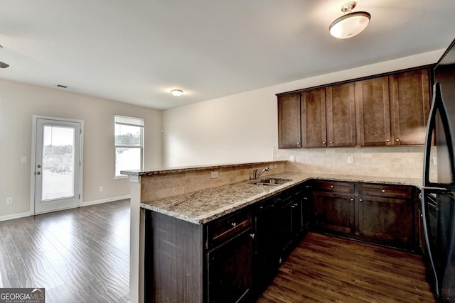 kitchen with kitchen peninsula, dark hardwood / wood-style floors, light stone counters, and black fridge