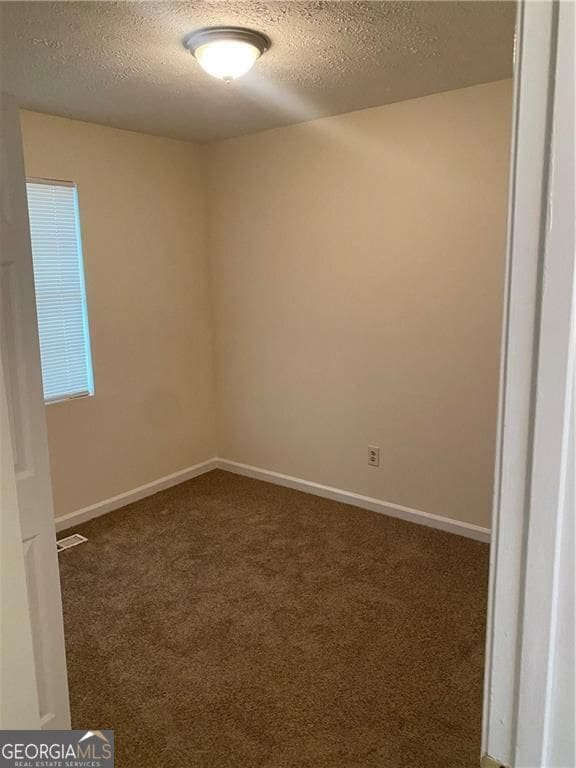 carpeted spare room with visible vents, a textured ceiling, and baseboards