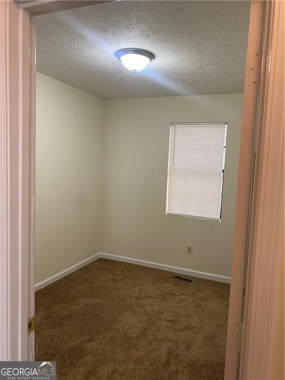 carpeted spare room featuring baseboards, visible vents, and a textured ceiling