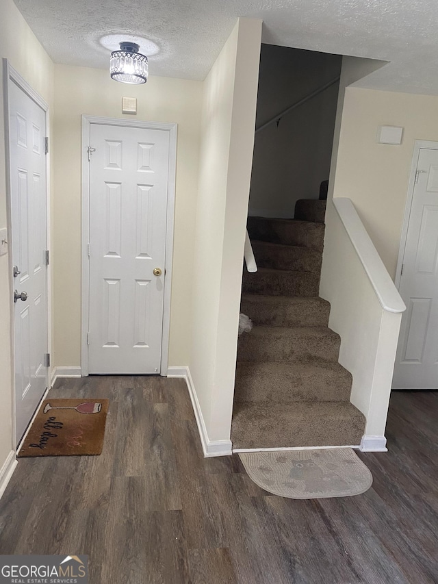 entryway featuring stairs, wood finished floors, baseboards, and a textured ceiling