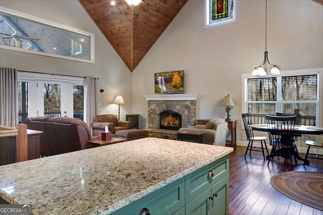 living room with dark wood-type flooring, a stone fireplace, wood ceiling, a chandelier, and high vaulted ceiling