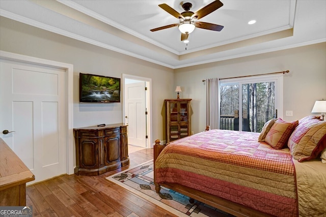 bedroom featuring hardwood / wood-style flooring, ornamental molding, a tray ceiling, and access to exterior