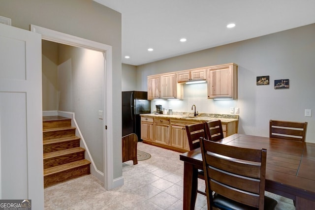 kitchen featuring light brown cabinetry, sink, light tile patterned floors, light stone counters, and black fridge