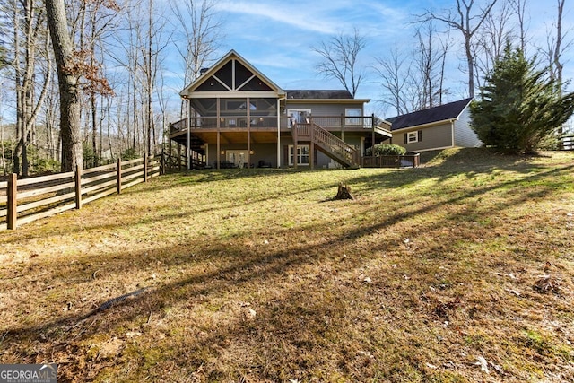 back of property with a sunroom, a deck, and a lawn