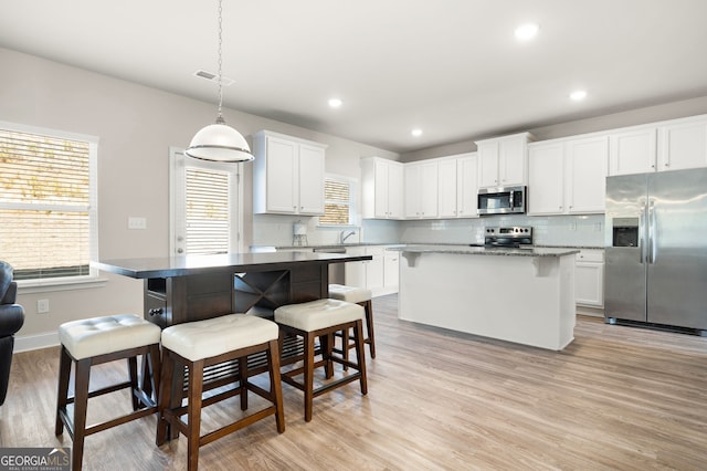 kitchen with a kitchen island, white cabinetry, hanging light fixtures, appliances with stainless steel finishes, and a kitchen bar