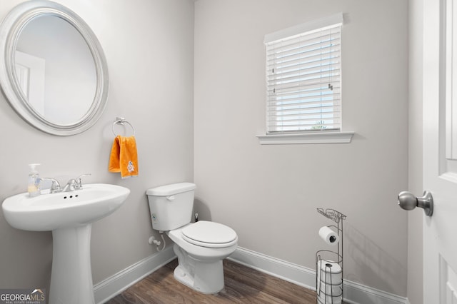 half bath featuring a sink, toilet, baseboards, and wood finished floors