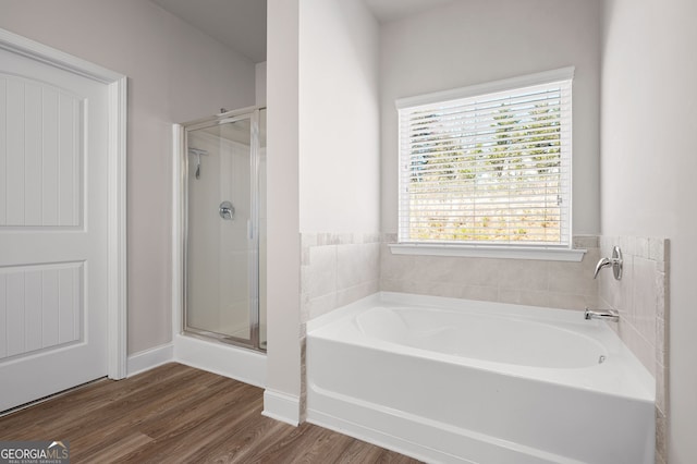 bathroom featuring a stall shower, wood finished floors, a bath, and baseboards