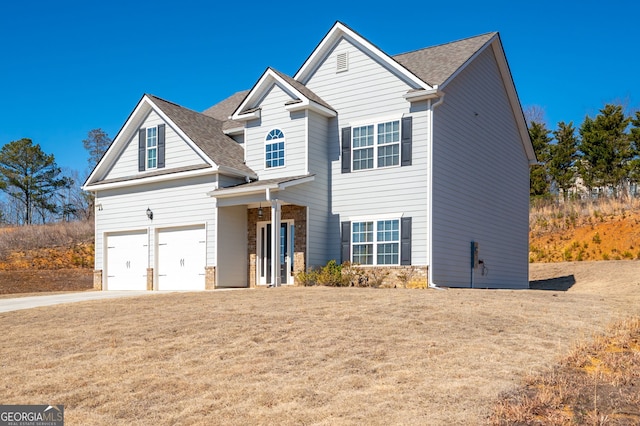 traditional-style house with a shingled roof, a front yard, concrete driveway, and stone siding