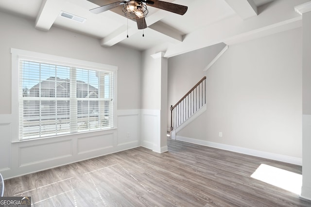 empty room featuring light wood-style floors, beam ceiling, visible vents, and stairs