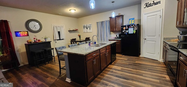 kitchen featuring sink, hanging light fixtures, dark hardwood / wood-style floors, black appliances, and a center island with sink