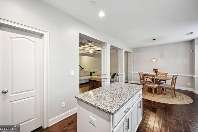 kitchen featuring pendant lighting, dark wood-type flooring, decorative columns, light stone countertops, and white cabinets