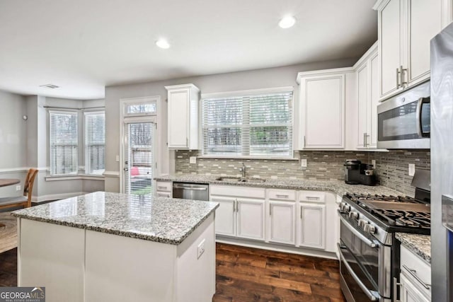 kitchen with sink, white cabinets, a center island, light stone counters, and stainless steel appliances