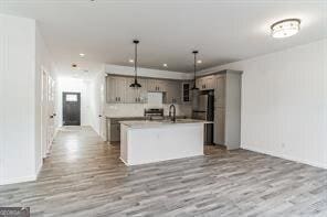 kitchen with decorative light fixtures, sink, a center island with sink, and light wood-type flooring