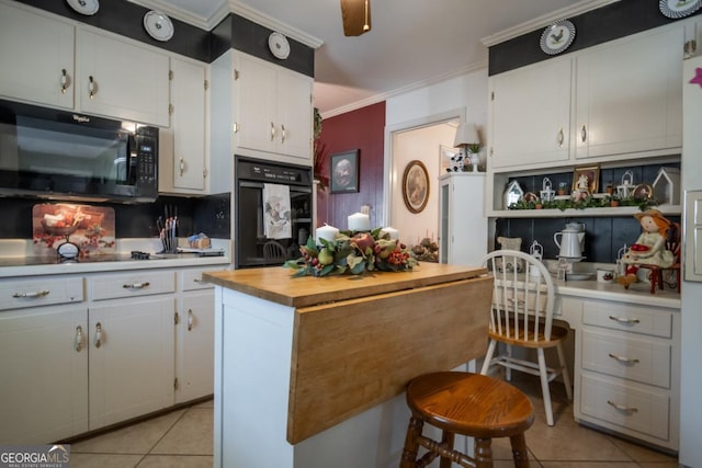 kitchen featuring a breakfast bar, built in desk, white cabinetry, light tile patterned floors, and black appliances