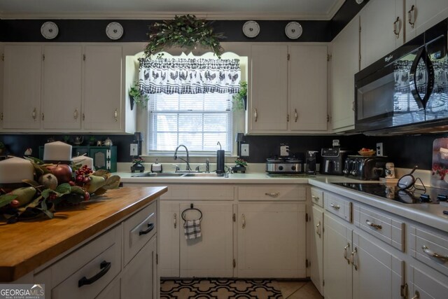 kitchen featuring ornamental molding, wood counters, white cabinets, black appliances, and a sink